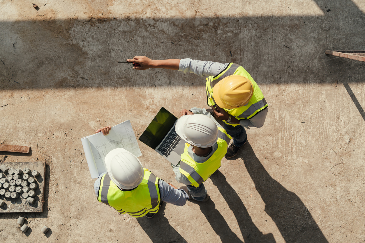 Three people in hi-vis vests and hard hats discussing potential water damage risk at a construction site.