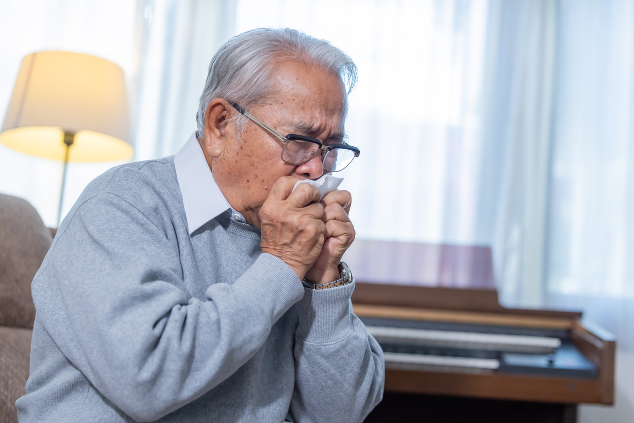 Older man coughing into a tissue indoors, a possible sign of mold-related air quality issues.