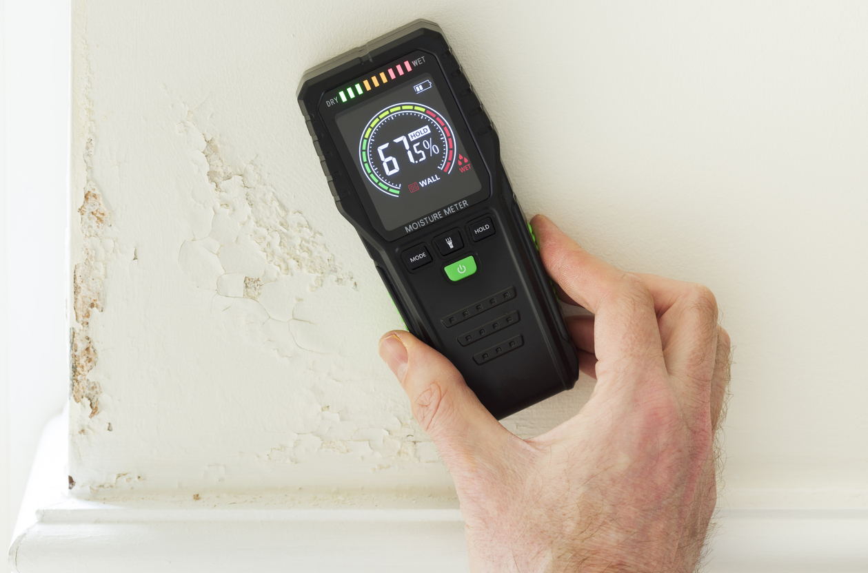 Restoration technician checking a wall for moisture with a meter in a water-damaged home